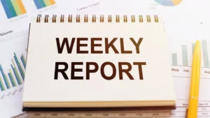 Spiral notepad labelled "Weekly Report" resting on printed sales graphs and bar charts, representing a VA weekly report template for tracking tasks and progress.